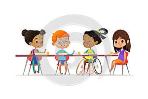 Girl in wheelchair sitting at table in canteen and talking to her friends. Happy multiracial kids having lunch. School inclusion c photo