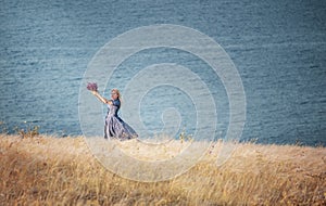 A girl whirling with a bouquet of wild flowers in her hands among the grass on a cliff by the sea. The atmosphere of happiness and