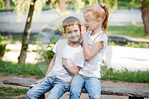 The girl whispers a secret in the ear. Children for a walk in the park.