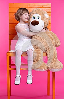 A girl whispers something in the ear of her huge toy bear