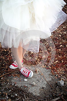 A girl in a white airy layered dress and red sneakers crossed her legs