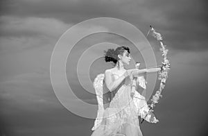 Girl in white angels dress, cupid with wings aiming with bow and arrow on a sky background. Valentines day concept