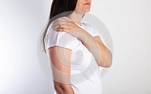 A girl on a white background is holding her shoulder and has aching pain. The concept of bursitis and pain of the