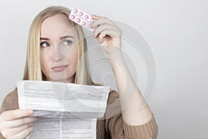 The girl on a white background reads the instructions for medicines. The woman looks at the list and composition of the drug. The