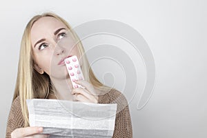 The girl on a white background reads the instructions for medicines. The woman looks at the list and composition of the drug. The