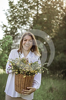 A girl in a white blouse holds a wicker basket with a bouquet of wild flowers. Summer walk in the field