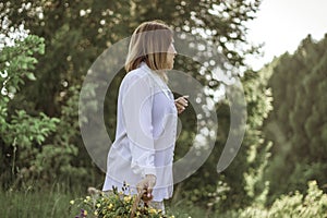 A girl in a white blouse holds a wicker basket with a bouquet of wild flowers. Summer walk in the field