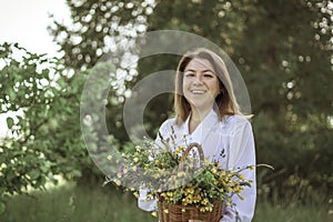 A girl in a white blouse holds a wicker basket with a bouquet of wild flowers. Summer walk in the field