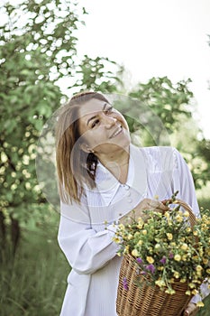 A girl in a white blouse holds a wicker basket with a bouquet of wild flowers. Summer walk in the field