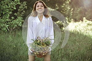 A girl in a white blouse holds a wicker basket with a bouquet of wild flowers. Summer walk in the field. midsection