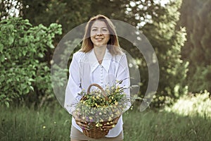 A girl in a white blouse holds a wicker basket with a bouquet of wild flowers. Summer walk in the field. midsection