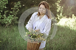 A girl in a white blouse holds a wicker basket with a bouquet of wild flowers. Summer walk in the field. midsection