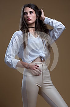 A girl in a white blouse and leather leggings on a beige background