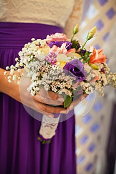 A girl in a white blouse and purple skirt holds in her hands a beautiful festive bouquet