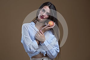 A girl in a white blouse with a ripe peach on a beige background