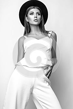 Girl in white clothes and black hat posing in studio on white background. Black and white photo