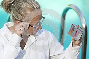 Girl in a white coat and glasses near the pool watching the tester checking the Ph and chlorine content in the water.