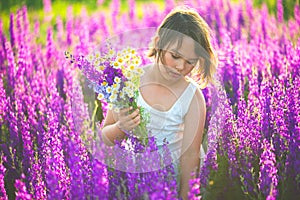 Girl in a white dress gathering purple flowers in summer