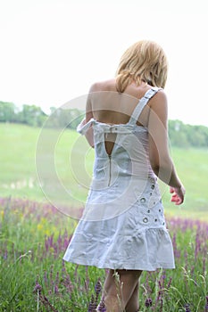 Girl in white dress going away on meadow