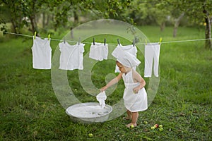 Girl in white dress hanging wet laundry to dry. Washing in a vintage basin.