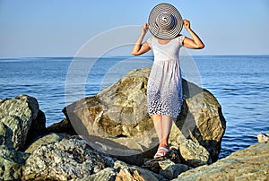 Girl in a white dress and with a hat on a rock by the sea