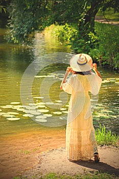 girl in a white dress and hat on the shore of a pond with water-lilies
