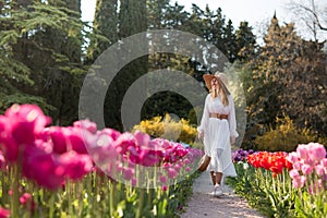 A girl in a white dress and hat walking in the middle of a field of beautiful multi-colored tulips.