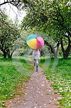 Girl in a white dress jumping in the blooming garden with colorful rainbow-umbrella. Spring, outdoors.