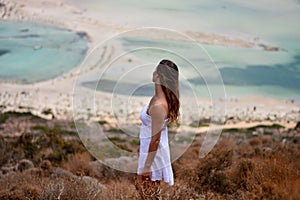 The girl in the white dress looks at the lagoon of Balos beach, Crete