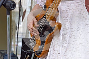 Girl in a white dress playing an electric bass guitar.