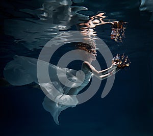 Girl in white dress posing under water with the boat