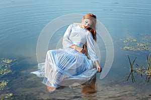 Girl white dress sitting on chair in a lake.