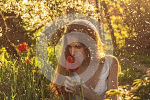 Girl in white dress smelling tulip in sunset among fluff, dandelions and cherry flowers