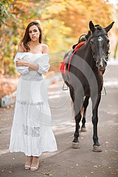 A girl in a white dress is standing with her back to the horse.