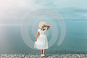 A girl in a white dress stands on the seashore