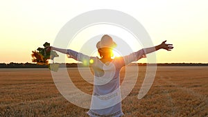 A girl in a white dress and a straw hat is holding a bouquet of flowers from a sunflower and raising her hands up. A