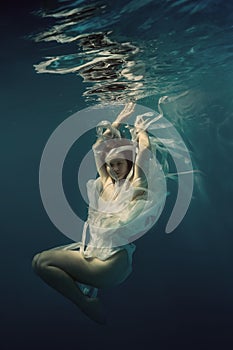 A girl in a white dress swims underwater as if flying in zero gravity