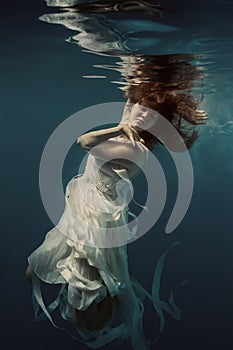 A girl in a white dress swims underwater as if flying in zero gravity