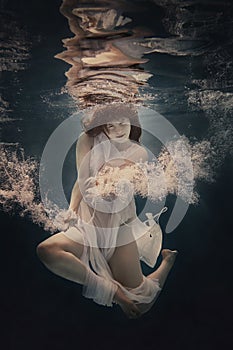 A girl in a white dress swims underwater as if flying in zero gravity