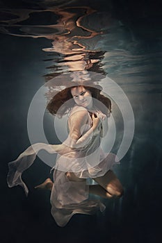 A girl in a white dress swims underwater as if flying in zero gravity