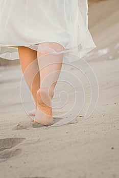 A girl in a white dress walking in the sand