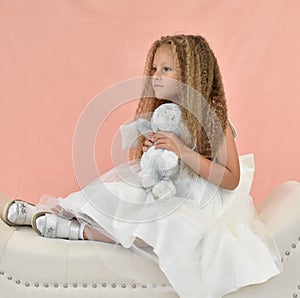 a girl in a white elegant dress with long hair holds a toy hare