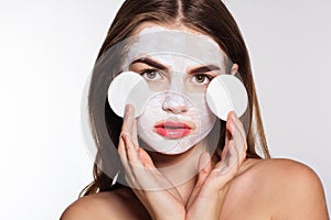 Girl with white face pack and cotton pads in hands