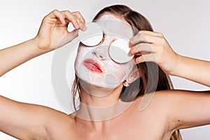 Girl with white face pack and cotton pads in hands