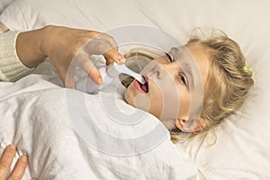 a girl with white hair lies in bed. mom using an inhaler makes an injection in the throat of a patient photo