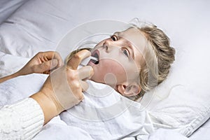 a girl with white hair lies in bed. mom using an inhaler makes an injection in the throat of a patient photo