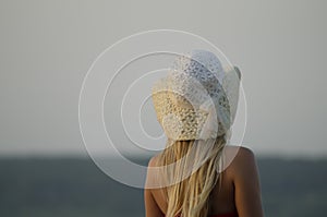 A girl with white hair in a summer hat stands near the sea