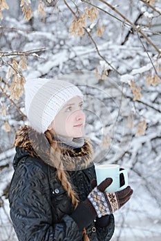 Girl in a white hat with cup of tea. Winter, outdoors. Side view