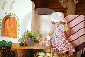 Girl in a white hat and a dress in a floral print with an apple for Easter