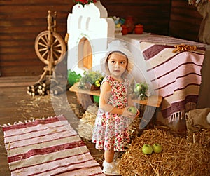 Girl in a white hat and a dress in a floral print with an apple for Easter